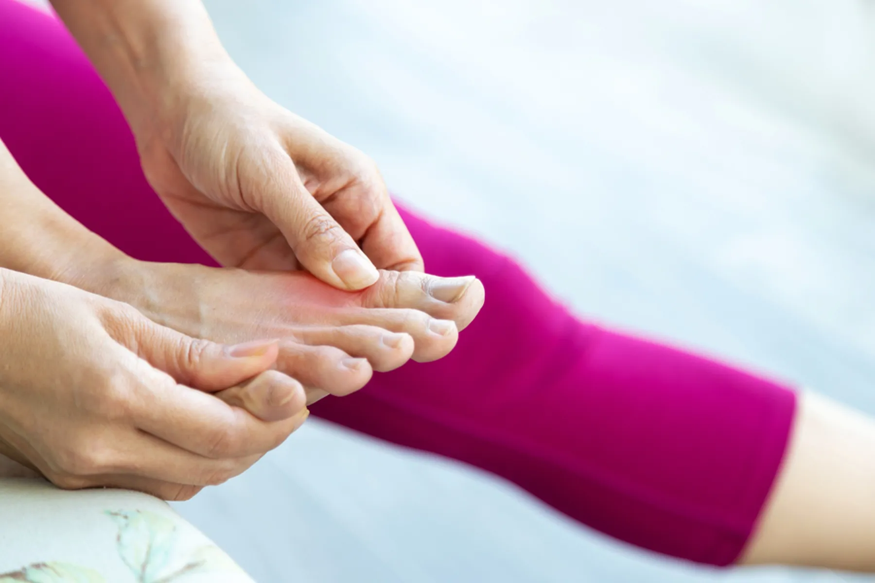 A woman in magenta workout pants holds her toes during a painful gout attack. 