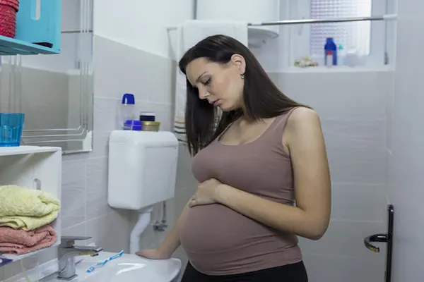 A pregnant woman holds her belly and makes a pained face.