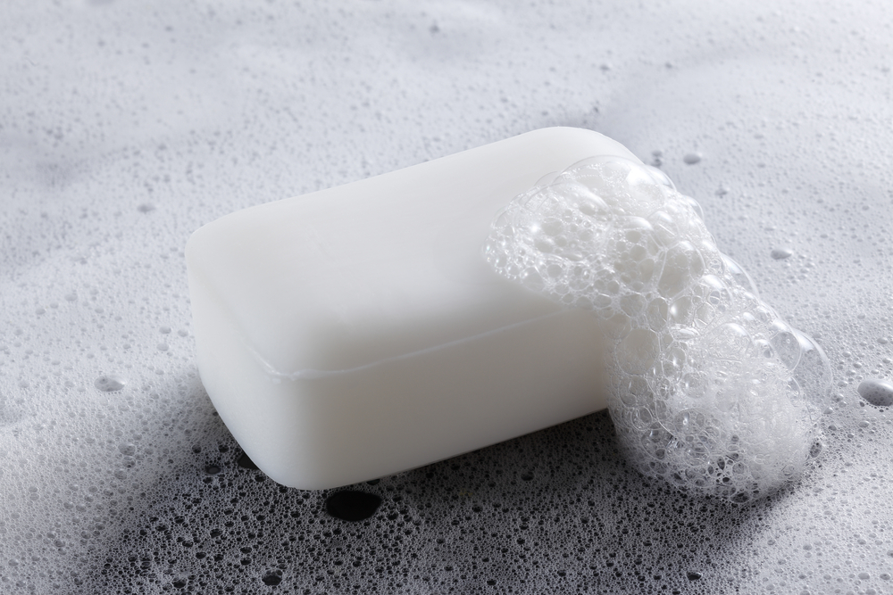 A white bar of soap sitting on a surface. There are some suds and bubbles next to the bar of soap. 