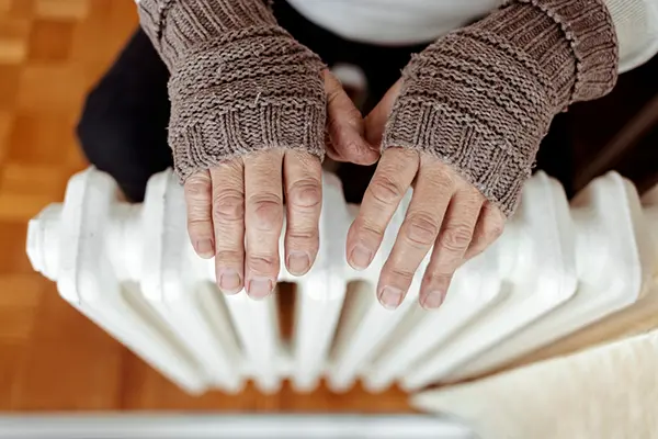 Person with fingerless gloves holding their hands over a radiator.