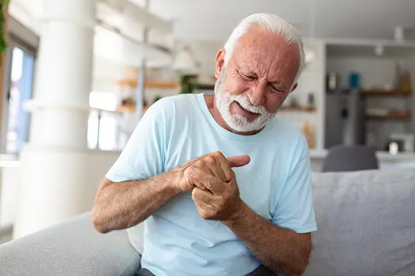 A man in a blue tee shirt holds his fingers and clenches his face in pain.