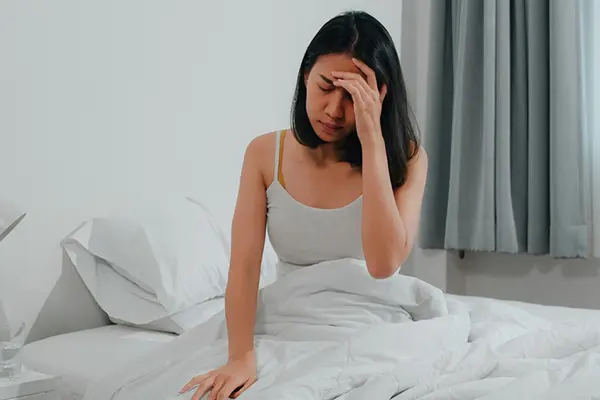 A woman sits in bed and holds her head.