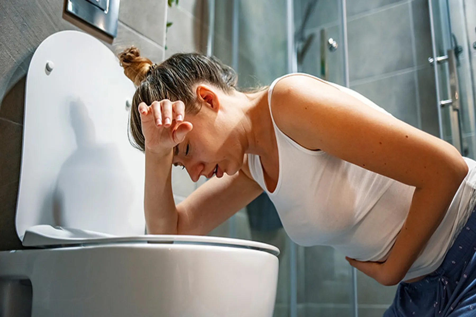 A woman leans over a toilet, about to vomit.