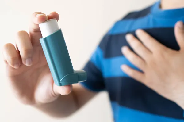 A young man in a blue striped shirt using a blue inhaler for asthma relief