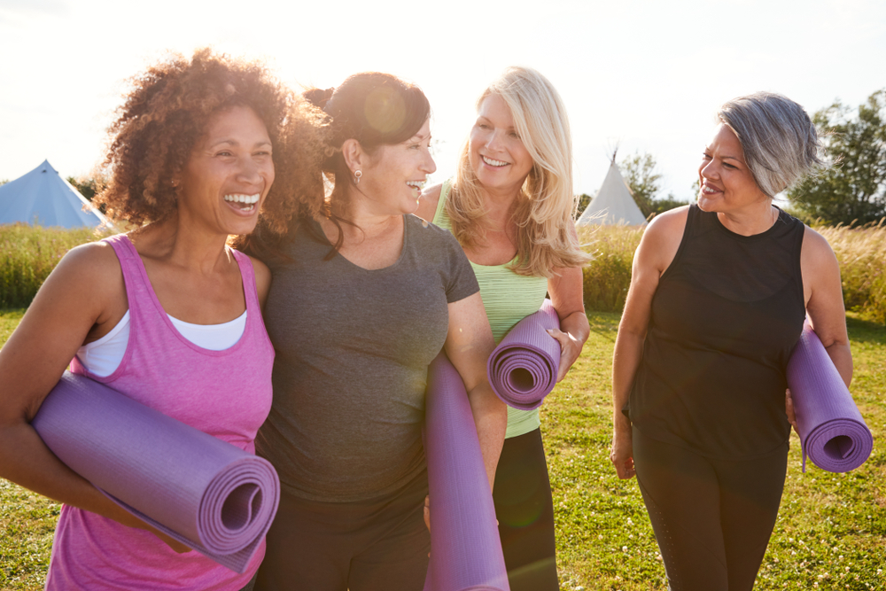 A group of older women laugh while holding yoga mats.