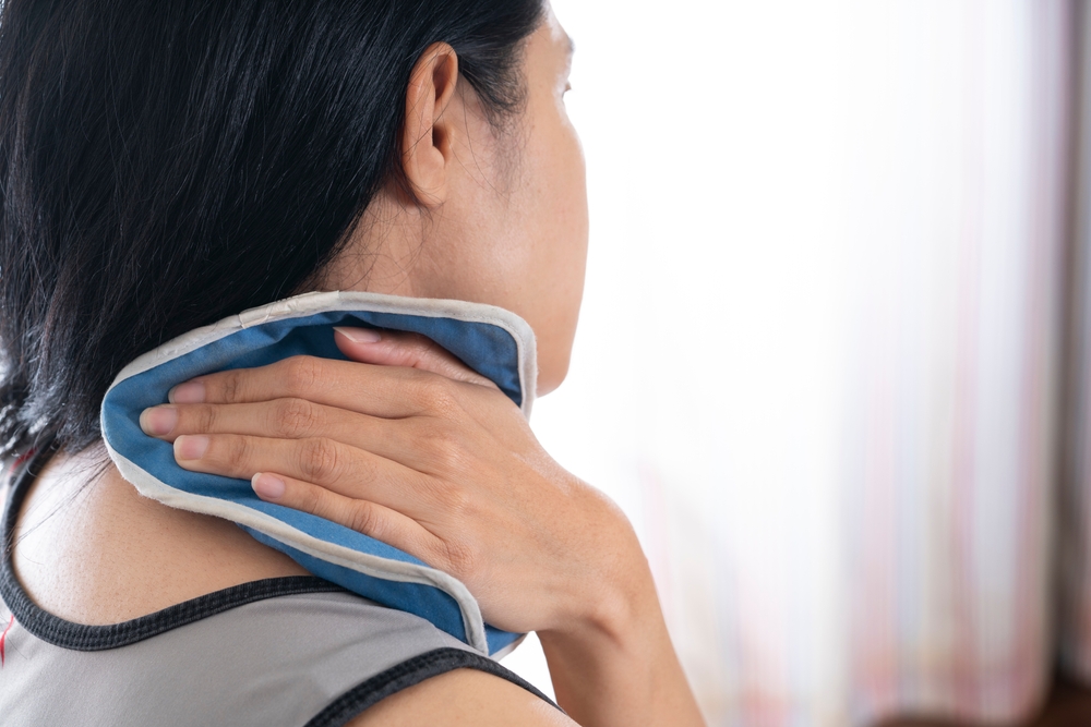 A woman holds a cold compress to the back of her neck.