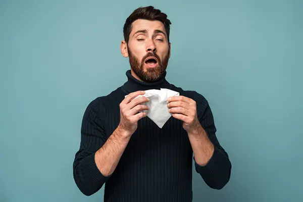 Man holding tissues in front of face, about to sneeze.