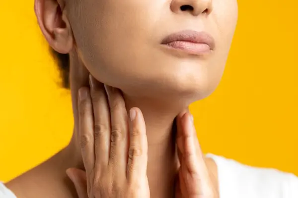 Woman holds her hands to her uncomfortable thyroid glands.