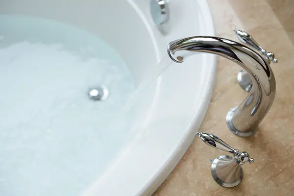 A luxury bathtub and faucet. The faucet is running, and the bathtub is partly filled up with water. 