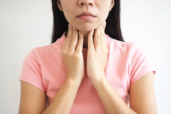 A woman feels her lymph nodes, implying she has a sore throat.