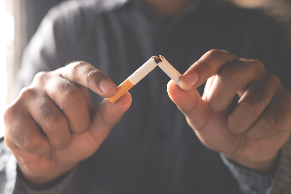 A man holding a cigarette toward the camera. The cigarette is broken in half as to represent quitting a smoking habit. 