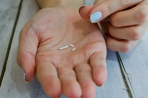 A woman's palm holding about a dozen medicine pellets.