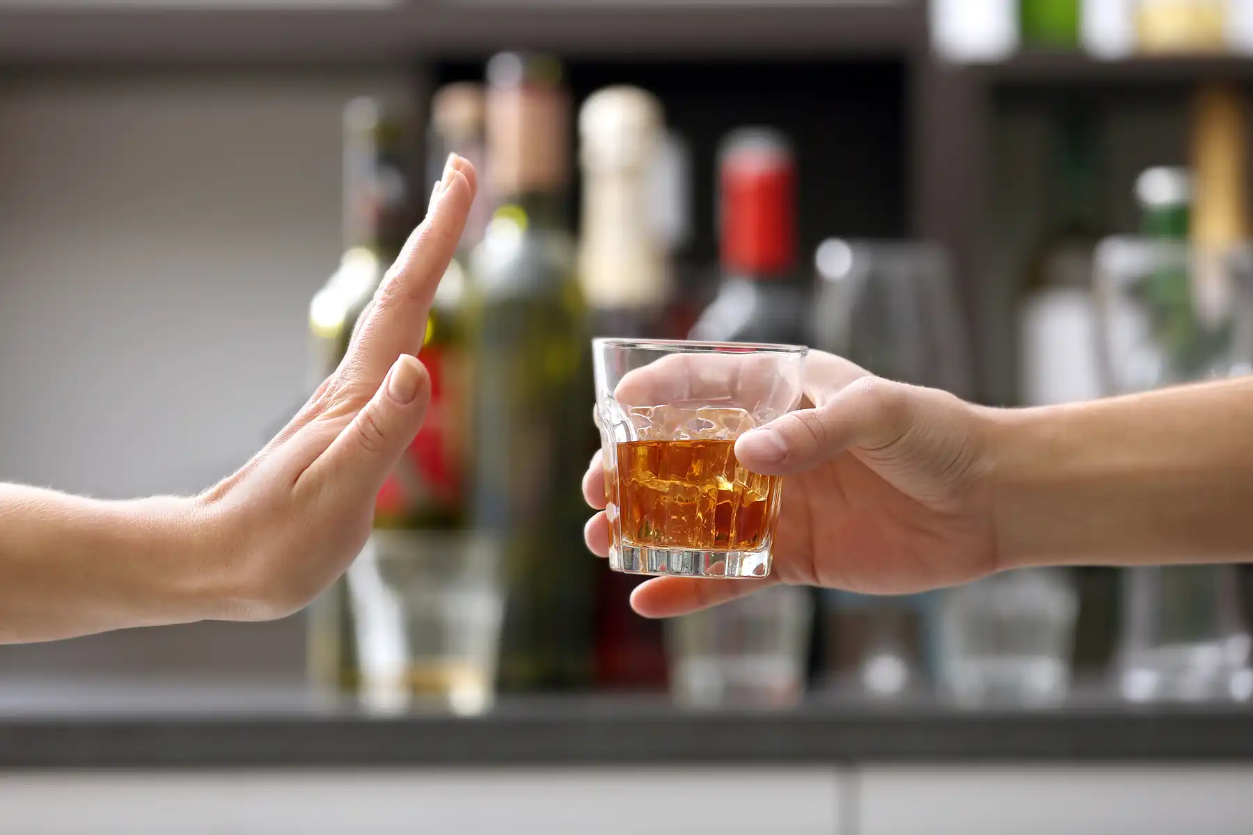 One hand extending a glass of whiskey, another hand extended signaling 