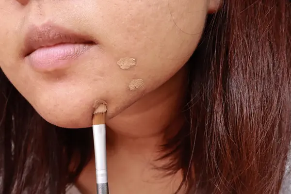 Woman applying concealer to specific spots on her face.