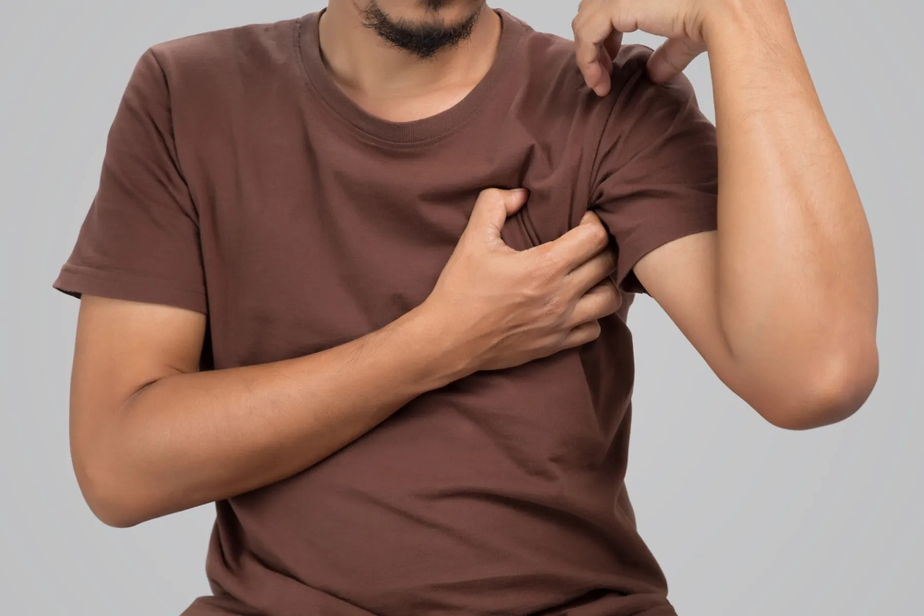 A man itches over his shirt in his armpit area.