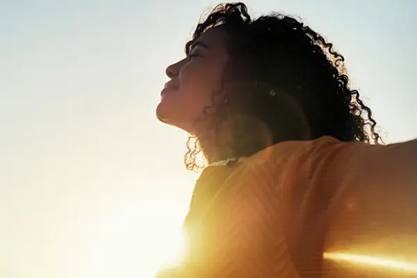 Woman with her eyes closed and her arms stretched out to her sides smiling and basking in the sun.