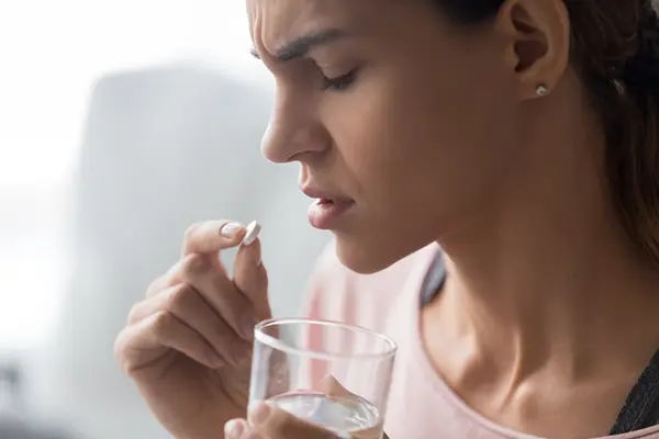 A woman holds a glass of water and takes a pill.