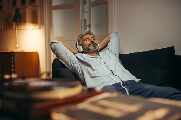 Man laying back on his couch and relaxing while listening to music on his headphones.