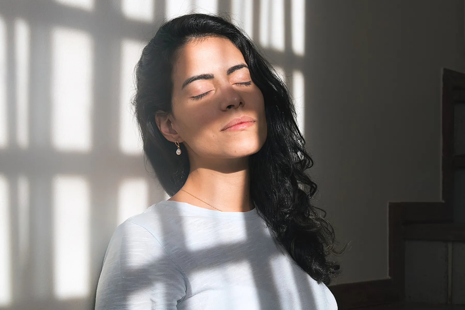 A woman lays against a wall with fractured sunlight hitting her.