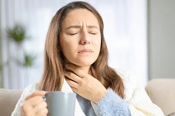 Woman experiencing throat pain and holding a cup of tea.