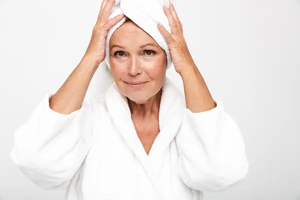 A woman in a bathrobe holds a towel on her head