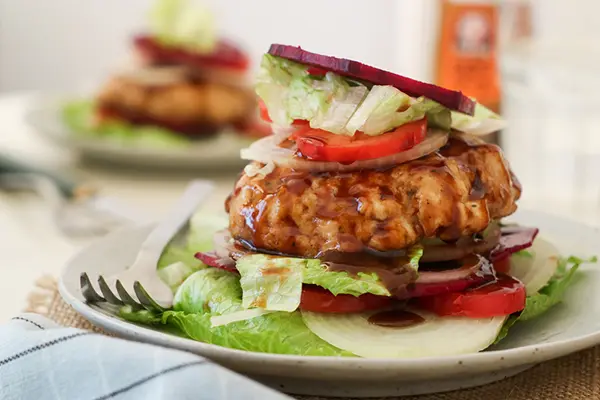 A low-carb burger with no bun. The burger is topped with lettuce, tomato, and onions. A fork sits to the side of the burger.