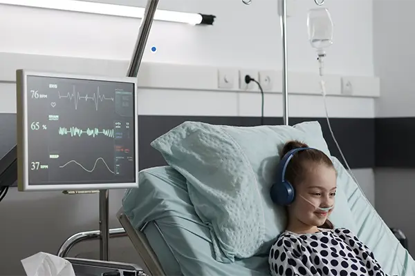 Young girl connected to an EKG machine with a nose cannula smiling with her headphones on. 