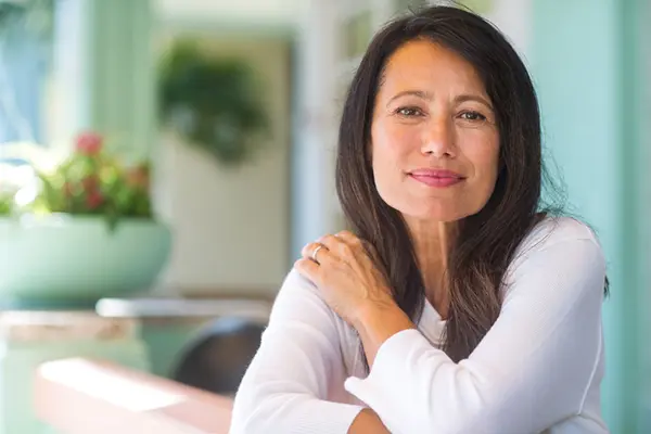 Middle-aged woman with straight black hair and a long-sleeved white shirt softly smiles at the camera.