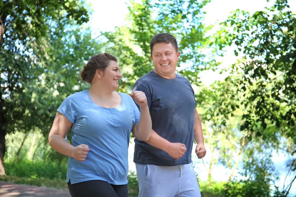 A man and woman smile at each other as they jog or speed walk outside. 