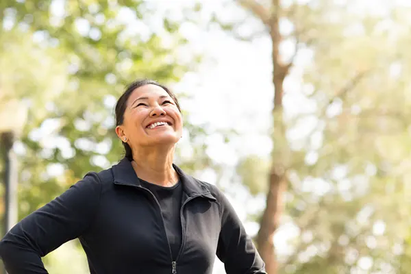 An Asian woman in a black shirt and black workout jacket is smiling up toward the sky. 