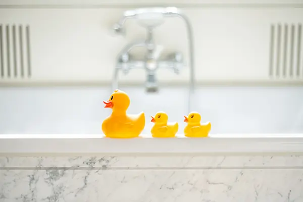 A close-up shot cute of three yellow rubber duckies on the ledge of a bathtub.