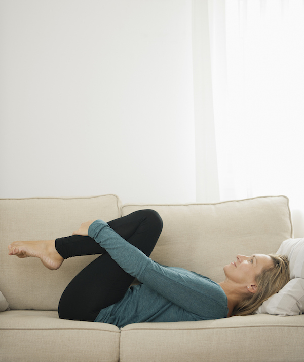 Mature woman lying on couch hugging knees