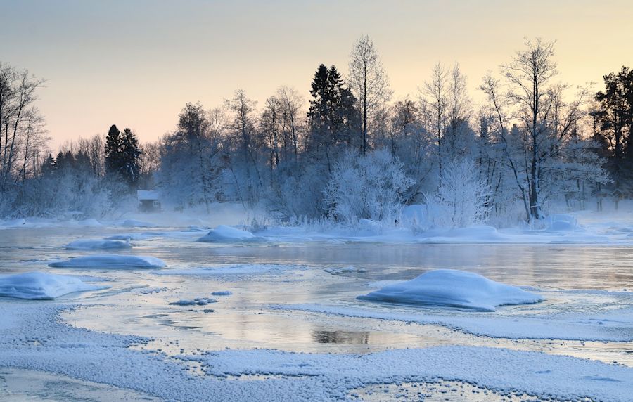 Osittain jäätynyt koski lumisen metsän ympäröivänä