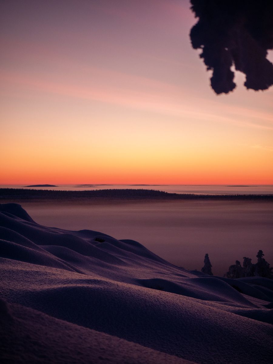 Auringonlasku usvaisella maisemalla lumisen mäen päältä