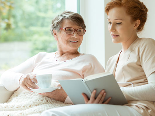 Ambulante Pflegekraft liest Seniorin vor.