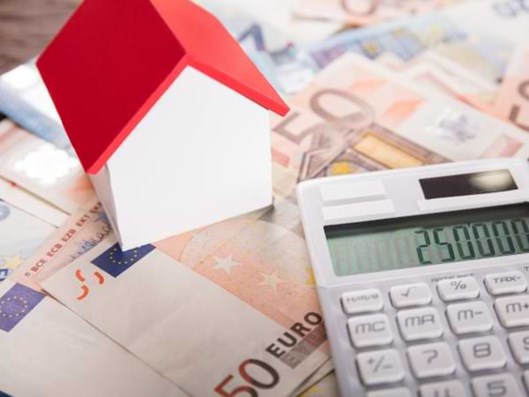 Miniaturhaus auf mehreren Geldscheinen. Ein Taschenrechner liegt daneben.