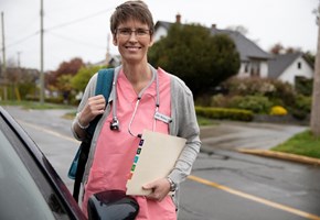 Ältere Pflegerin steht draußen mit Rucksack und Akte am Auto