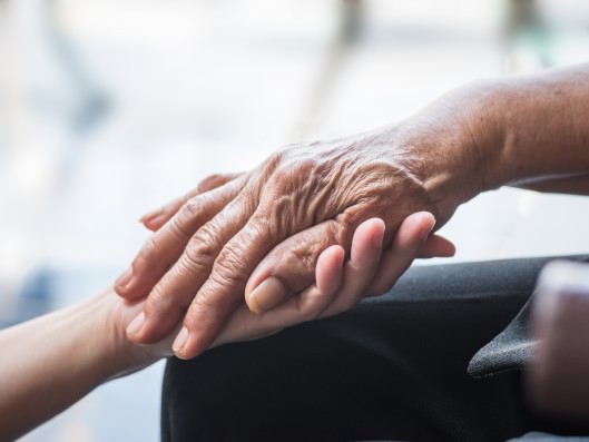 Eine helfende Hand liegt liebevoll auf einer anderen.
