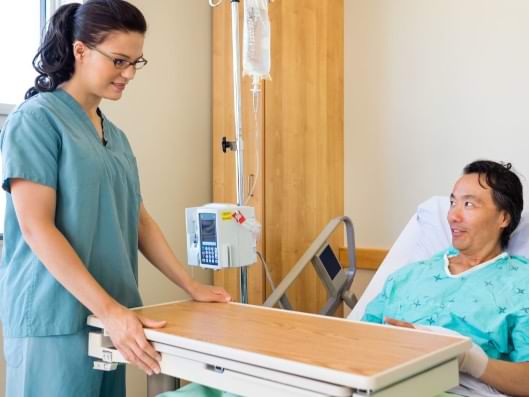 Patient liegt im Pflegebett mit Pflegebetttisch