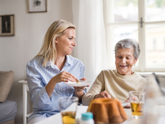 Senioren isst mit Seniorenbetreuungskraft Kuchen.