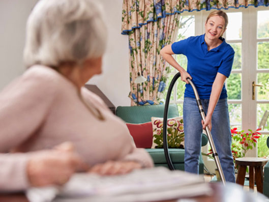 Haushaltshilfe saugt die Wohnung einer Seniorin.