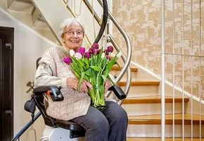 Seniorin mit Blumen sitzt auf dem Treppenlift 