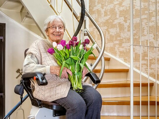 Seniorin mit Blumen sitzt auf dem Treppenlift_240x320