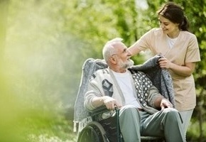 Senior im Rollstuhl wird von Pflegerin mit Decke zugedeckt