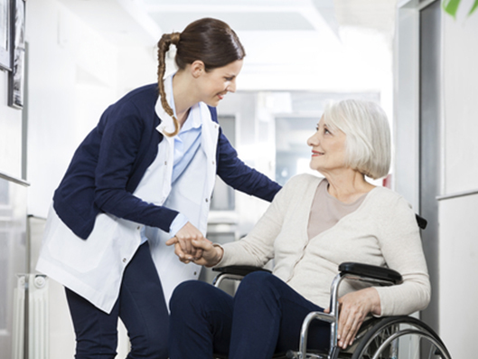 Pflegekraft heißt Seniorin willkommen.