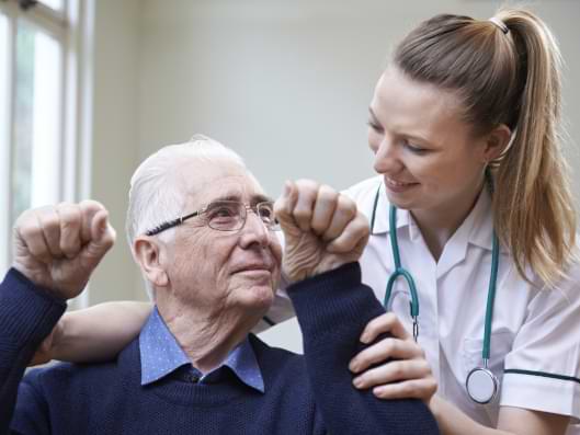 Eine Pflegekraft unterstützt einen Senioren bei rehabilitierenden Übungen.