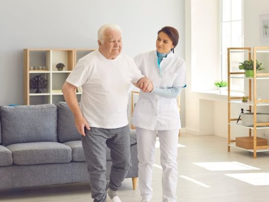 Pflegerin hält älteren Mann beim Gehen.