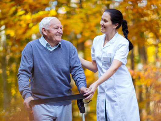 Pflegekraft geht mit Senior im Garten des Pflegeheims spazieren.