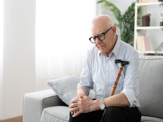 Mann sitzt mit Gehstock.