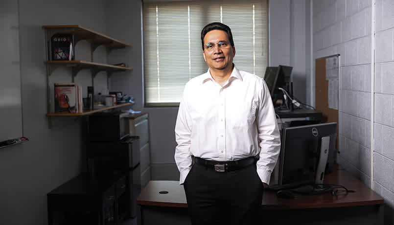Case School of Engineering Professor Vipin Chaudhary stands for a photo in his office wearing a white button up shirt and black pants. 
